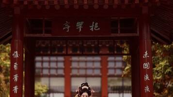 A traditional Chinese pavilion with a tiled roof and red pillars, featuring calligraphy and a person in traditional attire.