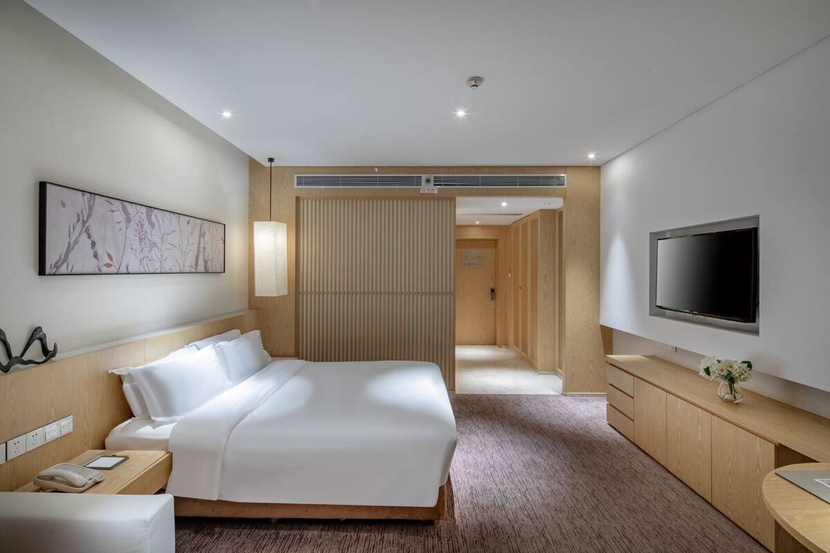 Une chambre d’hôtel moderne dotée d’un grand lit, de tables de chevet, d’un téléviseur à écran plat et d’un mur revêtu de panneaux en bois.