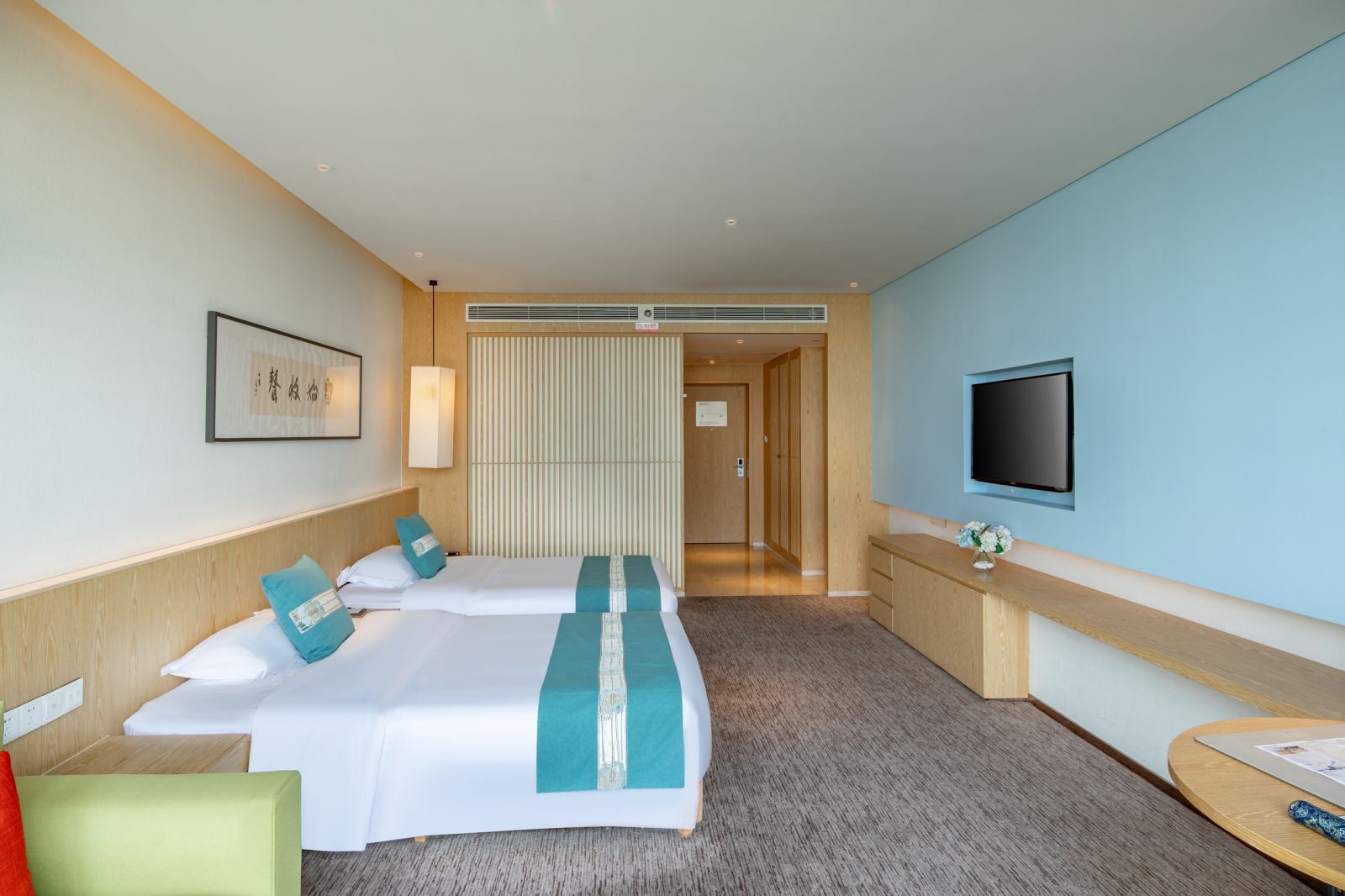 A hotel room with two beds, a TV, a desk, and a view of the hallway.