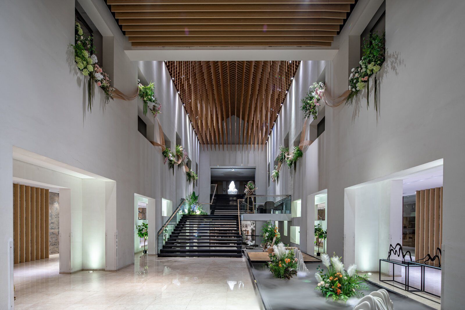 Amplo interior com escadaria central, elementos de design moderno e arranjos florais decorativos.