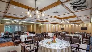 Un comedor de hotel con mesas redondas, sillas e iluminación colgante.
