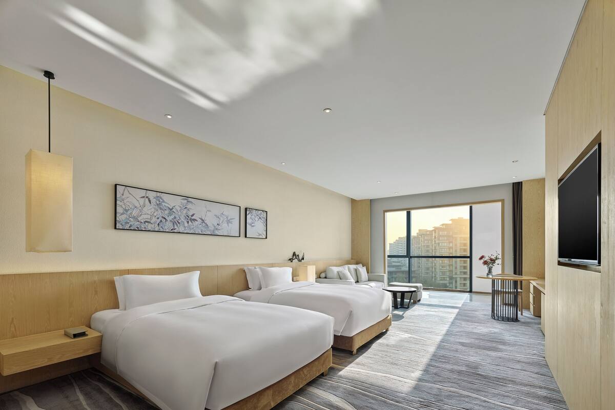 Une chambre d’hôtel moderne avec deux lits, une grande fenêtre et un téléviseur à écran plat.