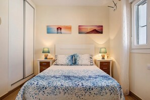 Une chambre à coucher comprenant un lit, deux tables de chevet, deux lampes fixées au mur et deux tableaux.