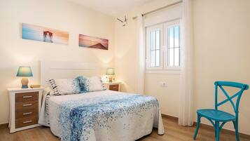 Een slaapkamer met een bed, twee nachtkastjes met lampen, een stoel en twee aan de muur hangende schilderijen.