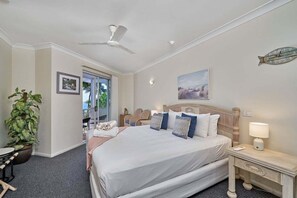 A hotel room with a bed, a ceiling fan, a clock, a plant, a desk, and a window. - Alassio Beachfront Apartment 302 (Palm Cove)