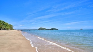 A beach with a pier extending into the water, a clear sky, and calm sea. - Absolute Beach Front 1 Bedroom Apartment Palm Cove (Cairns)