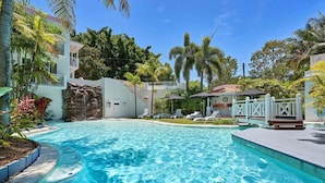 A swimming pool with lounge chairs, a waterfall feature, and tropical vegetation. - Absolute Beach Front 1 Bedroom Apartment Palm Cove (Cairns)