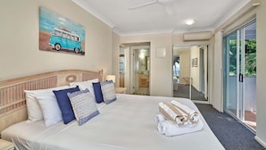 A hotel room with a bed, a ceiling fan, a painting of a van, and a view through a glass door. - Absolute Beach Front 1 Bedroom Apartment Palm Cove (Cairns)