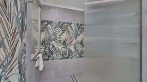 Une douche avec une porte en verre, un mur carrelé orné d’un motif de feuilles et un porte-serviettes.