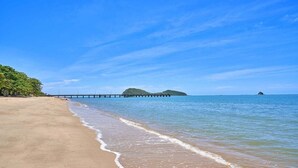 Une plage avec une jetée qui s’avance dans l’eau, un rivage sablonneux et un ciel dégagé.