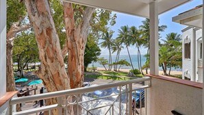 Un balcon avec vue sur une plage, des palmiers et un ciel dégagé.