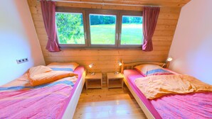Une petite chambre accueillante, avec deux lits, une fenêtre avec des rideaux et une vue sur un paysage verdoyant.