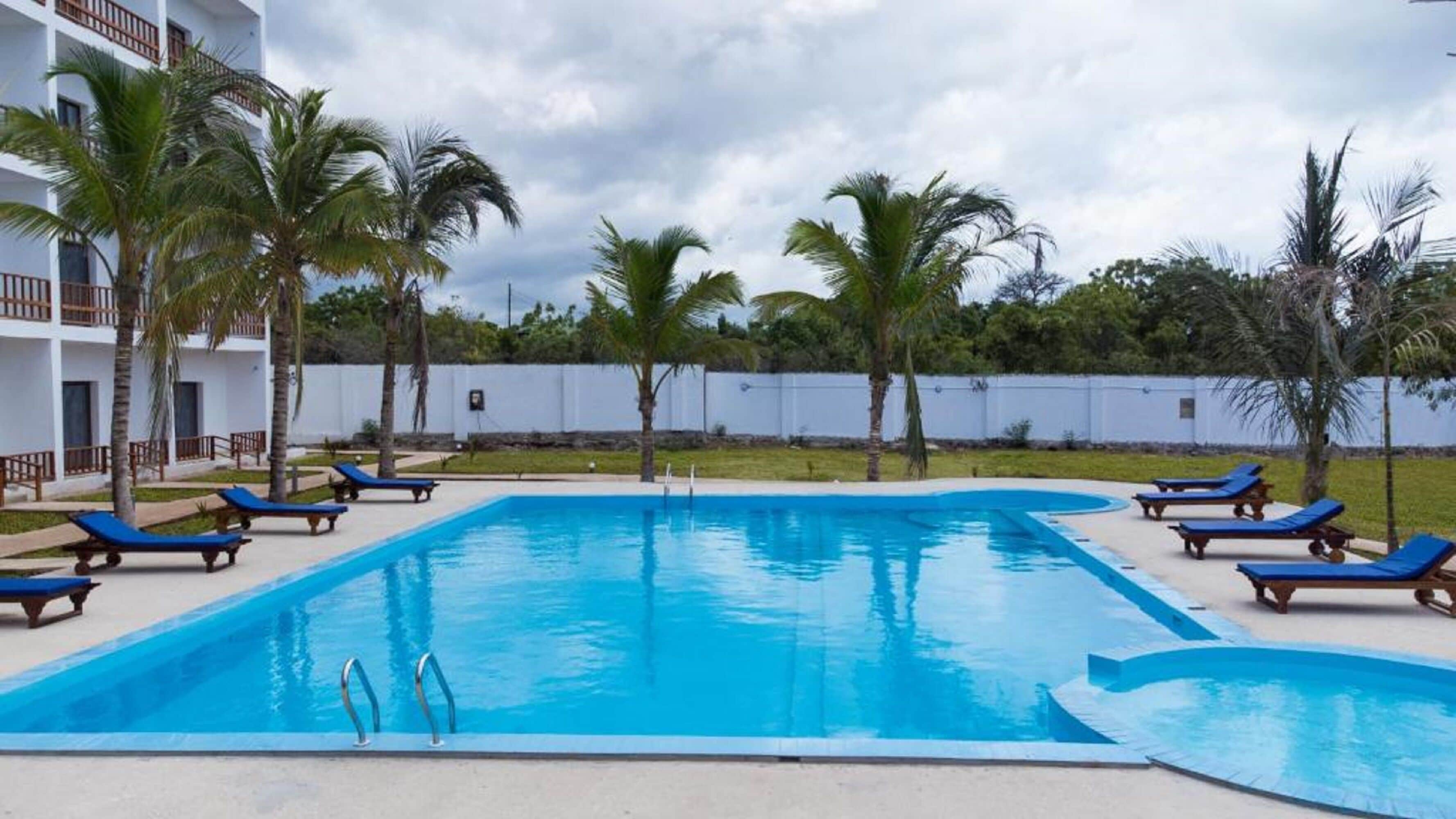 A rectangular swimming pool with clear blue water, surrounded by lounge chairs and palm trees.