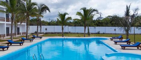 A rectangular swimming pool with clear blue water, surrounded by lounge chairs and palm trees.