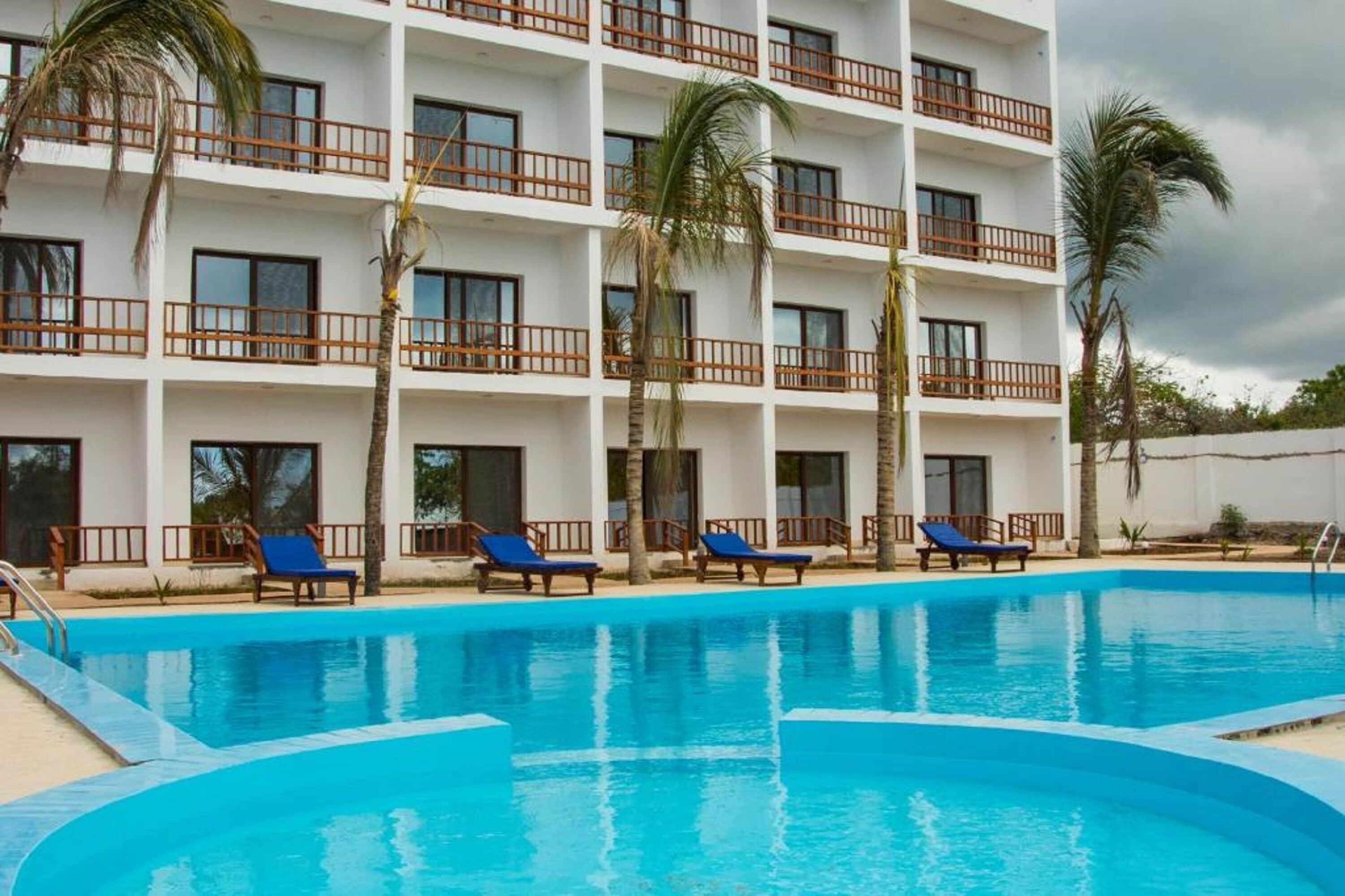 Un hotel con piscina, varios balcones y palmeras.