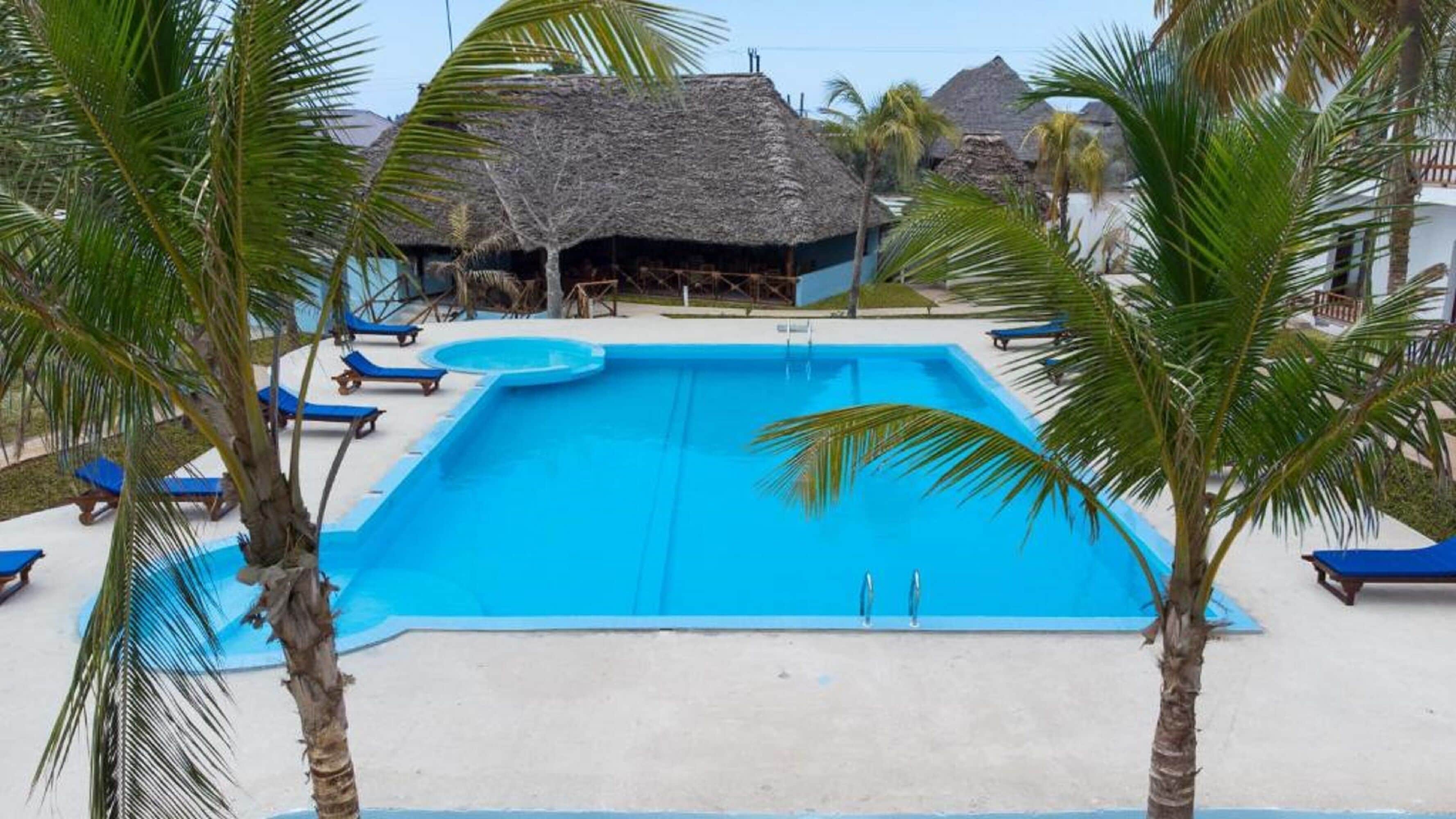 A swimming pool with lounge chairs and palm trees.