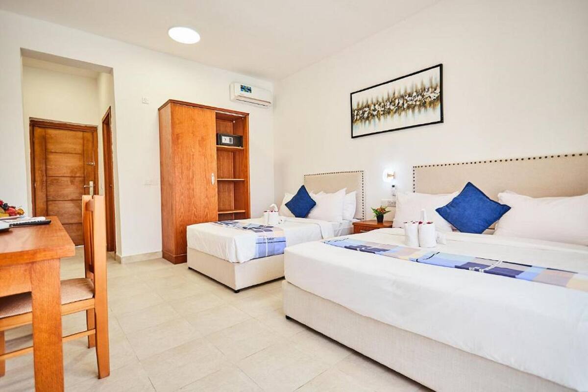 Una habitación de hotel con dos camas, un armario de madera, un escritorio y un cuadro en la pared.