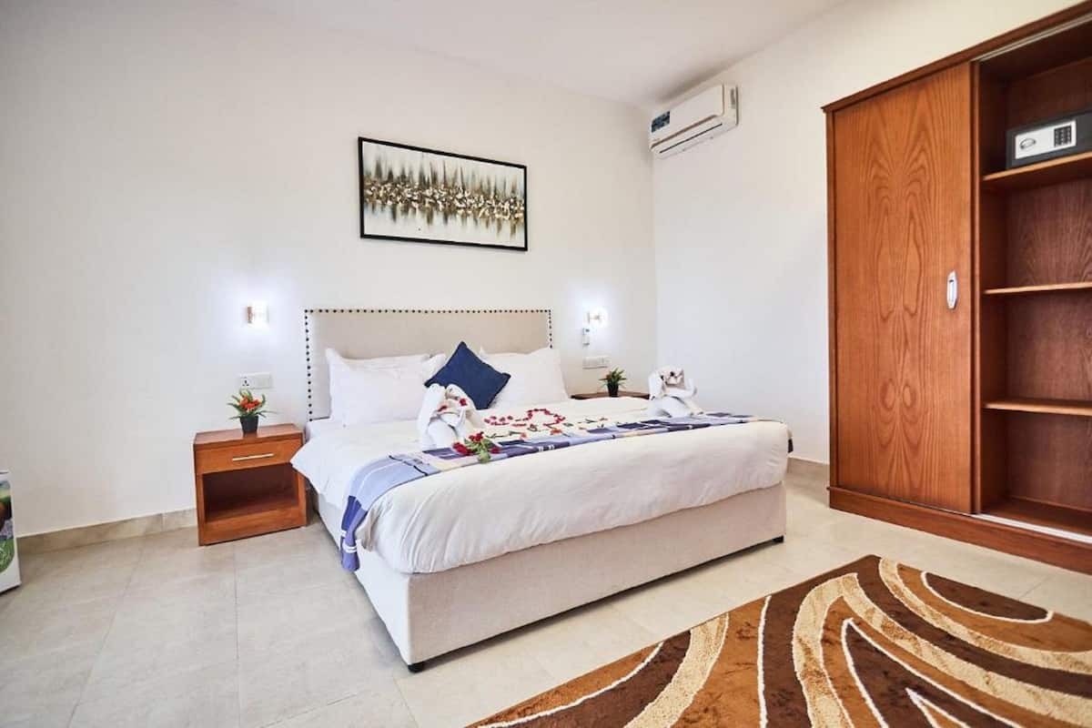 Un dormitorio con una cama grande, mesitas de noche, un armario y un cuadro enmarcado en la pared.