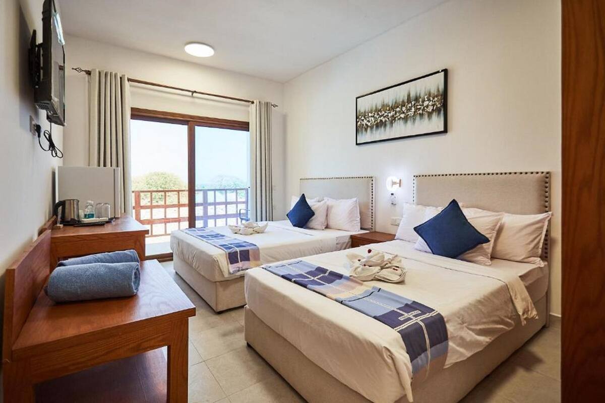 Habitación de hotel con dos camas, un escritorio, un televisor y un balcón con vistas.