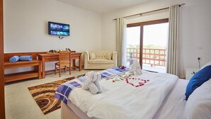 A hotel room with a bed, a desk, a chair, a television, and a balcony with curtains.