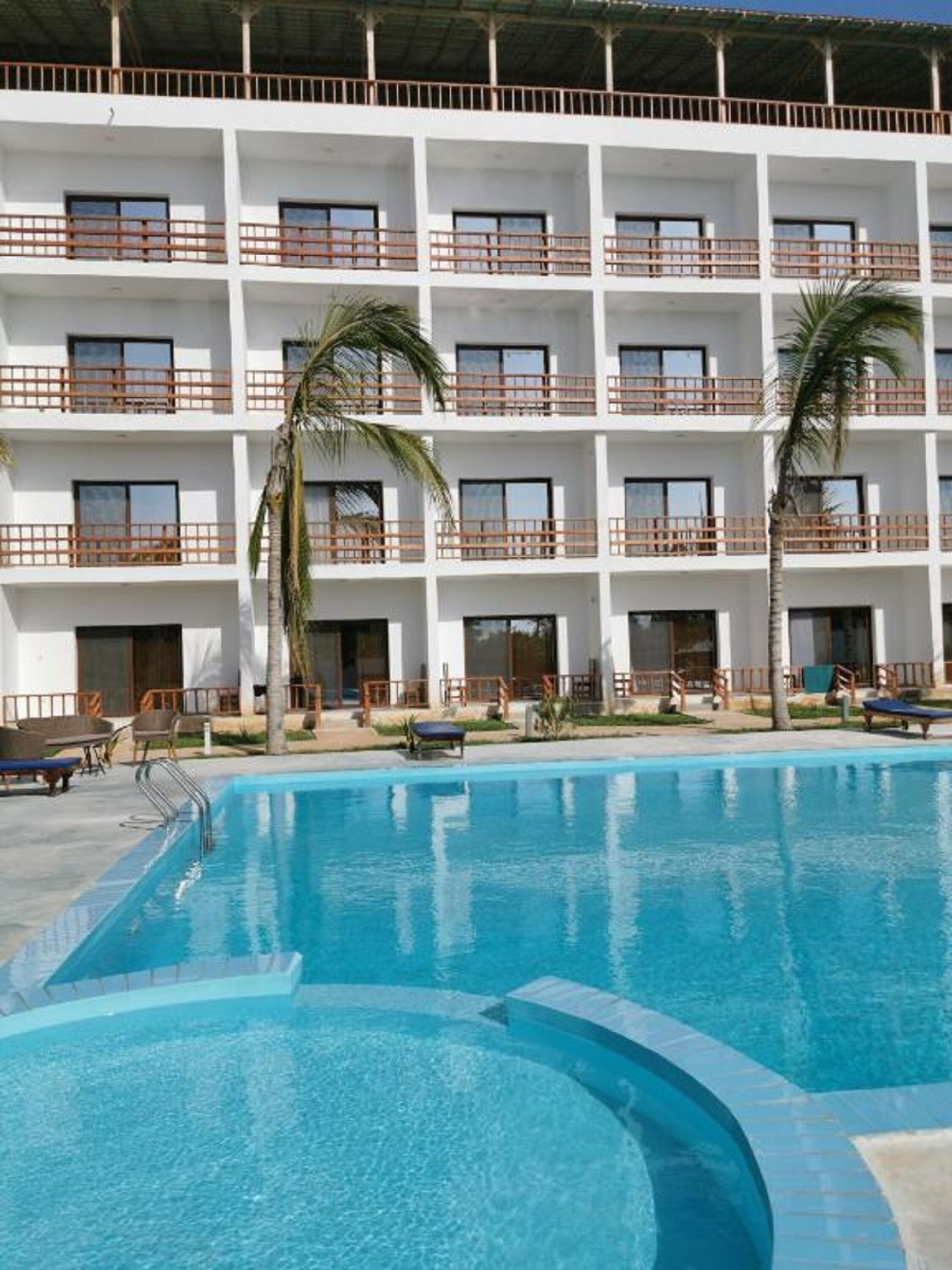 A hotel with a swimming pool, multiple balconies, and palm trees.
