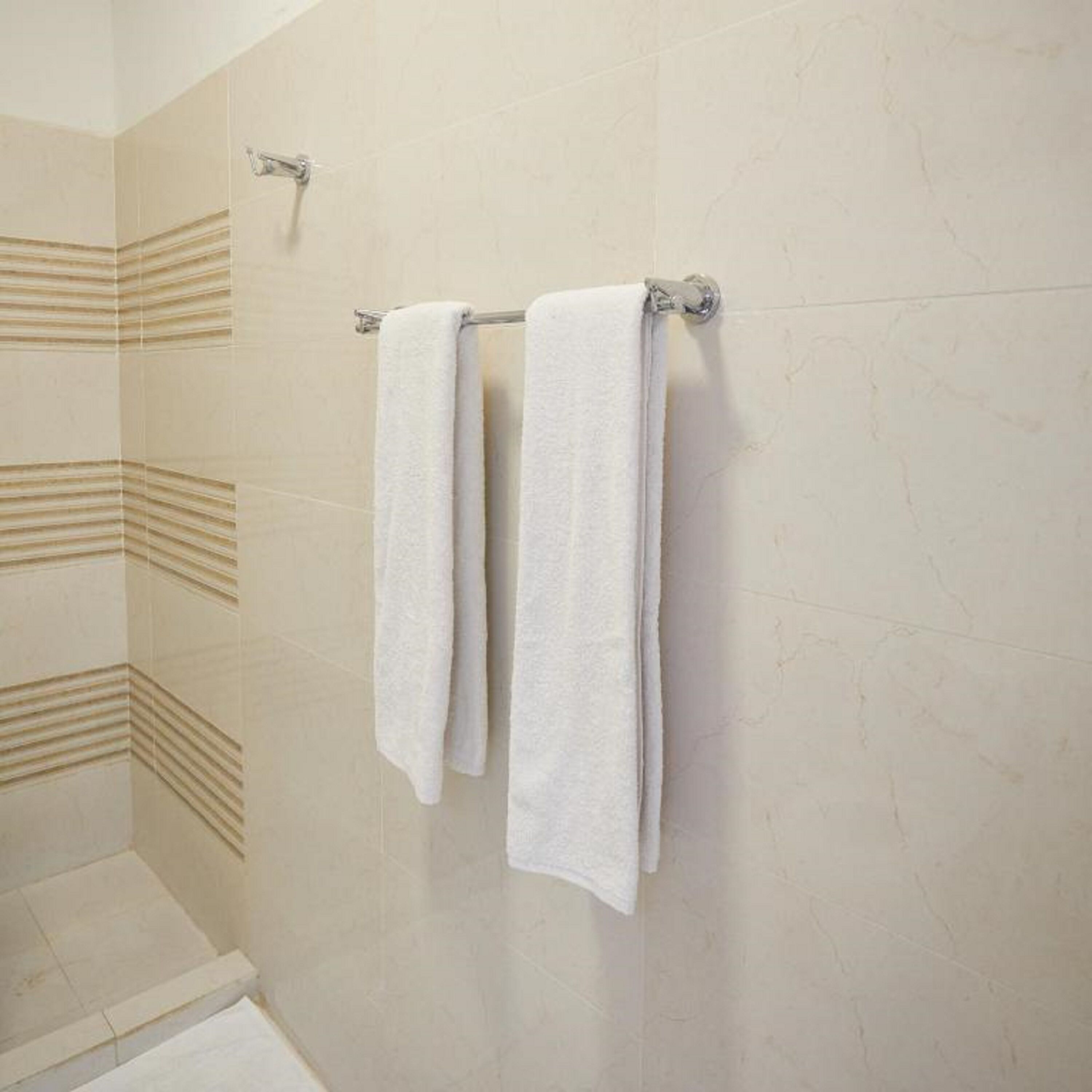 A bathroom with two white towels hanging on a metal towel rack against a tiled wall.