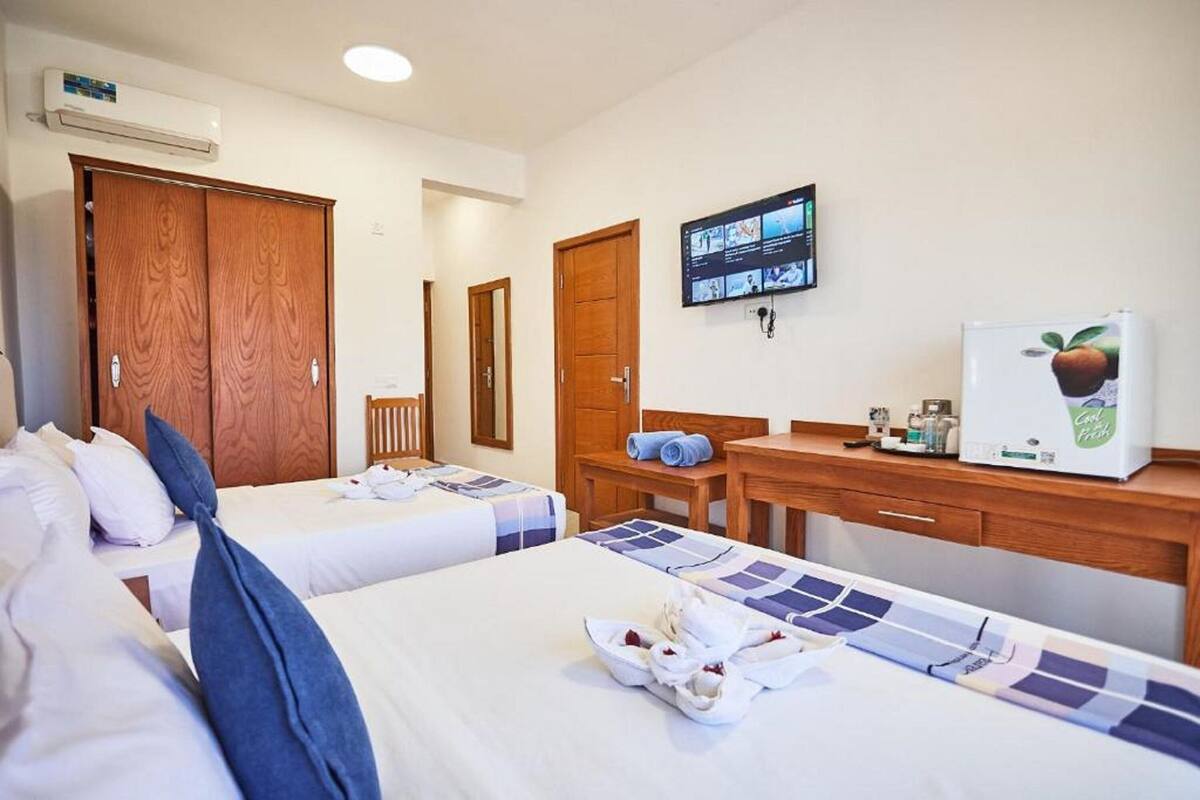 Una habitación de hotel con dos camas, un escritorio con refrigerador, televisión y armario.