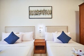 Quarto de hotel com duas camas, uma mesa de cabeceira, uma luminária fixada na parede e um quadro emoldurado sobre as camas.
