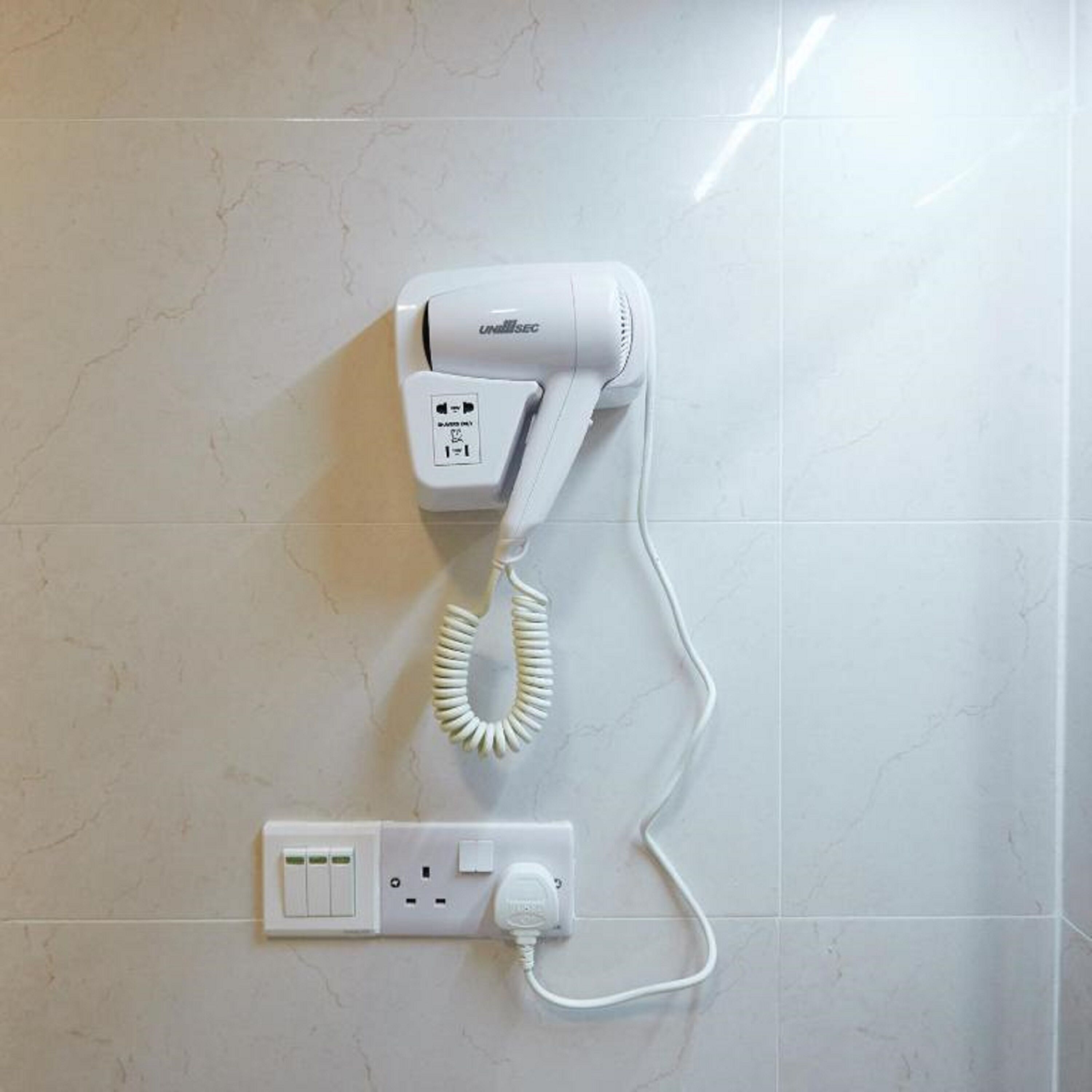 A hairdryer mounted on a wall with a power outlet below it.