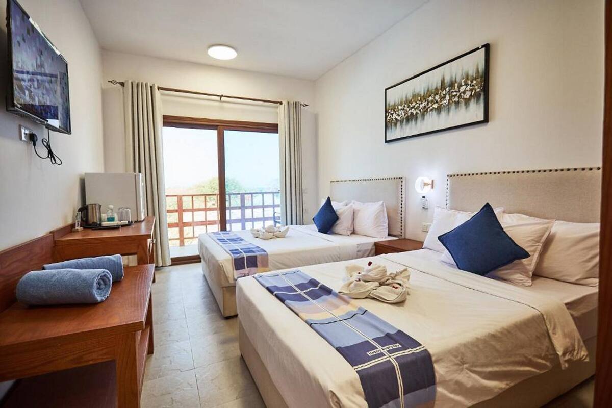 Habitación de hotel con dos camas, televisión, escritorio y balcón.
