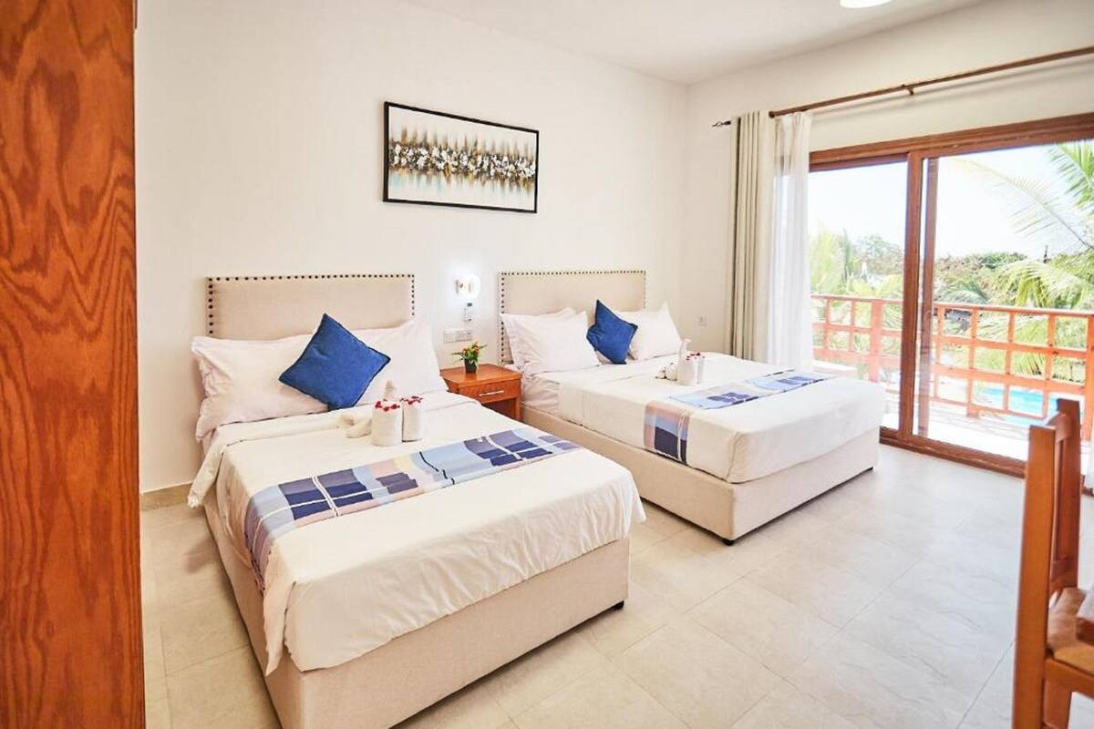 Habitación de hotel con dos camas, piso de madera, un ventanal con vistas y un cuadro en la pared.