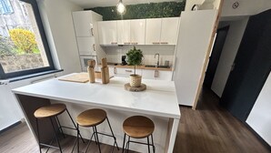 A modern kitchen with white cabinets, a central island with stools, a window with a view, and a green plant on the counter. - High comfort accommodation | Le Puy en Velay (Le Puy-en-Velay)