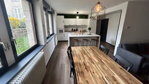 A modern kitchen with white cabinets, a wooden dining table, and a view of a garden through the window. - High comfort accommodation | Le Puy en Velay (Le Puy-en-Velay)
