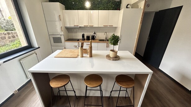 A modern kitchen with white cabinets, a central island with stools, a hanging light fixture, and a view of the outdoors through a window. - High comfort accommodation | Le Puy en Velay (Le Puy-en-Velay)