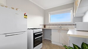 Pieni, käytännöllinen keittiö, jossa on jääkaappi, liesi, mikroaaltouuni ja ikkuna tiskialtaan yläpuolella.