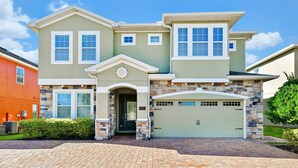 A two-story house with a stone facade, a green garage door, and a brick driveway.