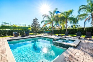 A rectangular swimming pool with a tiled edge, surrounded by a brick patio. There are lounge chairs and a small hot tub area.