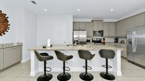 A modern kitchen with a central island, bar stools, stainless steel appliances, and a decorative wall piece.
