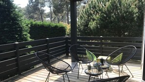 A covered outdoor area with a wooden deck, black metal chairs, and a glass table with two cups. - 4-bedroom family house with sauna, garden and terrace - near south beach (Lacanau)