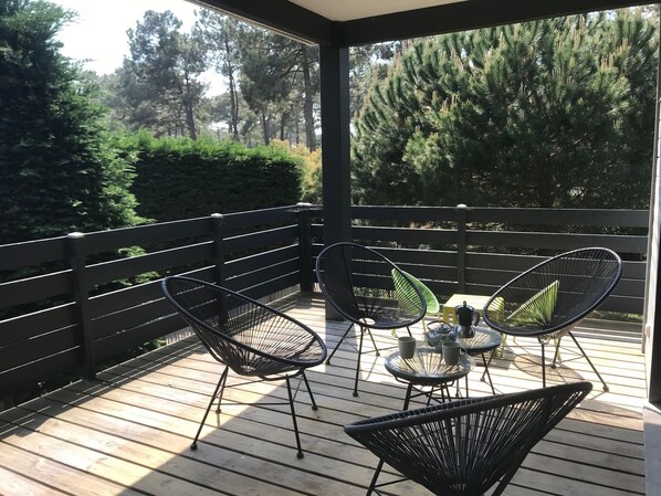 Un espace extérieur abrité, doté d’une terrasse en bois, de chaises en métal noir et d’une table en verre avec deux tasses.