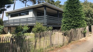 A two-story house with a balcony, surrounded by a wooden fence and trees. - 4-bedroom family house with sauna, garden and terrace - near south beach (Lacanau)