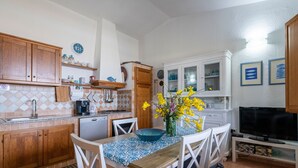 A kitchen with wooden cabinets, a dining table with chairs, a coffee maker, and a TV. - Holiday Home "Casa del Sole" with Sea View, Pool, Garden & Wi-Fi (TERTENIA)