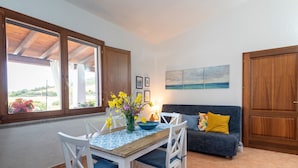 A dining area with a table and chairs, a vase with flowers, a sofa with cushions, and a painting on the wall. - Holiday Home "Casa del Sole" with Sea View, Pool, Garden & Wi-Fi (TERTENIA)