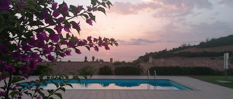 A swimming pool with a view of the sunset, surrounded by greenery and buildings.