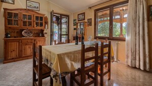 A dining area with a table set for four, wooden cabinets, and a window with curtains. - Holiday Home "Lilliu" with Mountain View, Garden & Air Conditioning (VILLACIDRO)