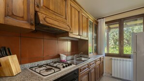 A kitchen with wooden cabinets, a gas stove, a sink, and a window with a view of greenery. - Holiday Home "Lilliu" with Mountain View, Garden & Air Conditioning (VILLACIDRO)