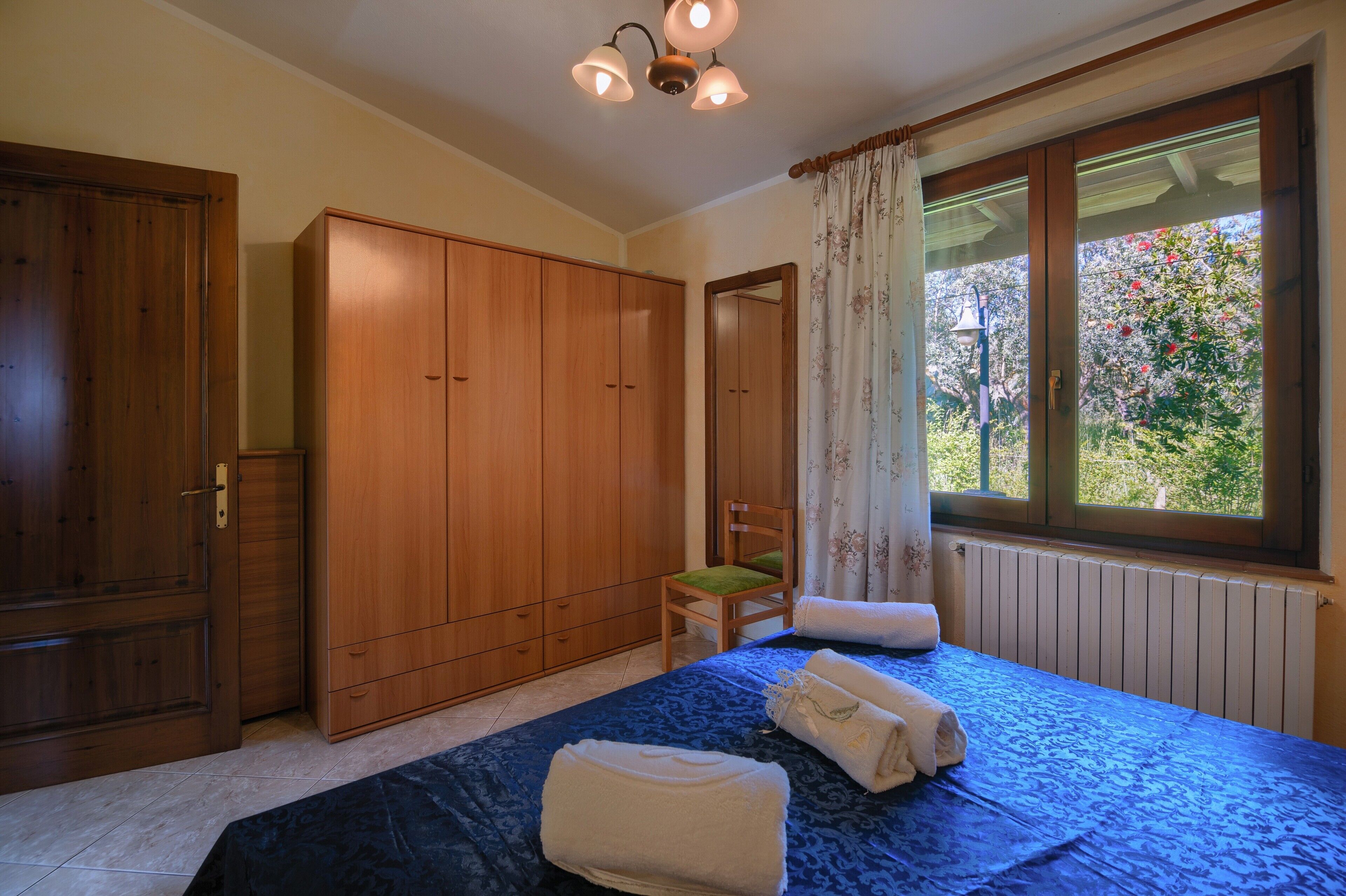 Une chambre à coucher comprenant un lit, une chaise, une armoire et une fenêtre donnant sur un paysage verdoyant.