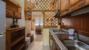 A kitchen with wooden cabinets, a gas stove, a sink, and a dining area with a table and chairs. - Holiday Home "Lilliu" with Mountain View, Garden & Air Conditioning (VILLACIDRO)