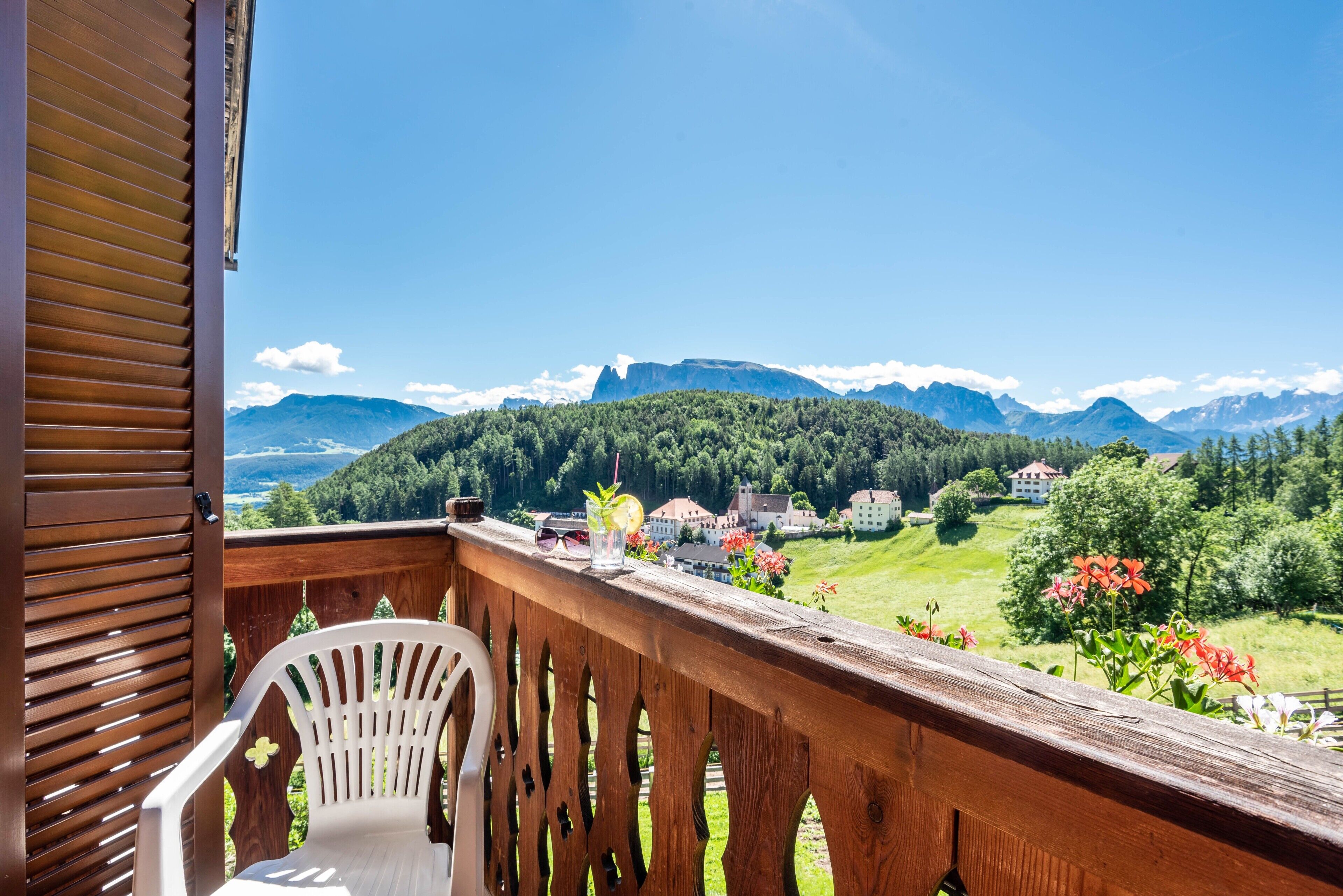 A balcony with a wooden railing, a white chair, and a scenic view of mountains and houses.