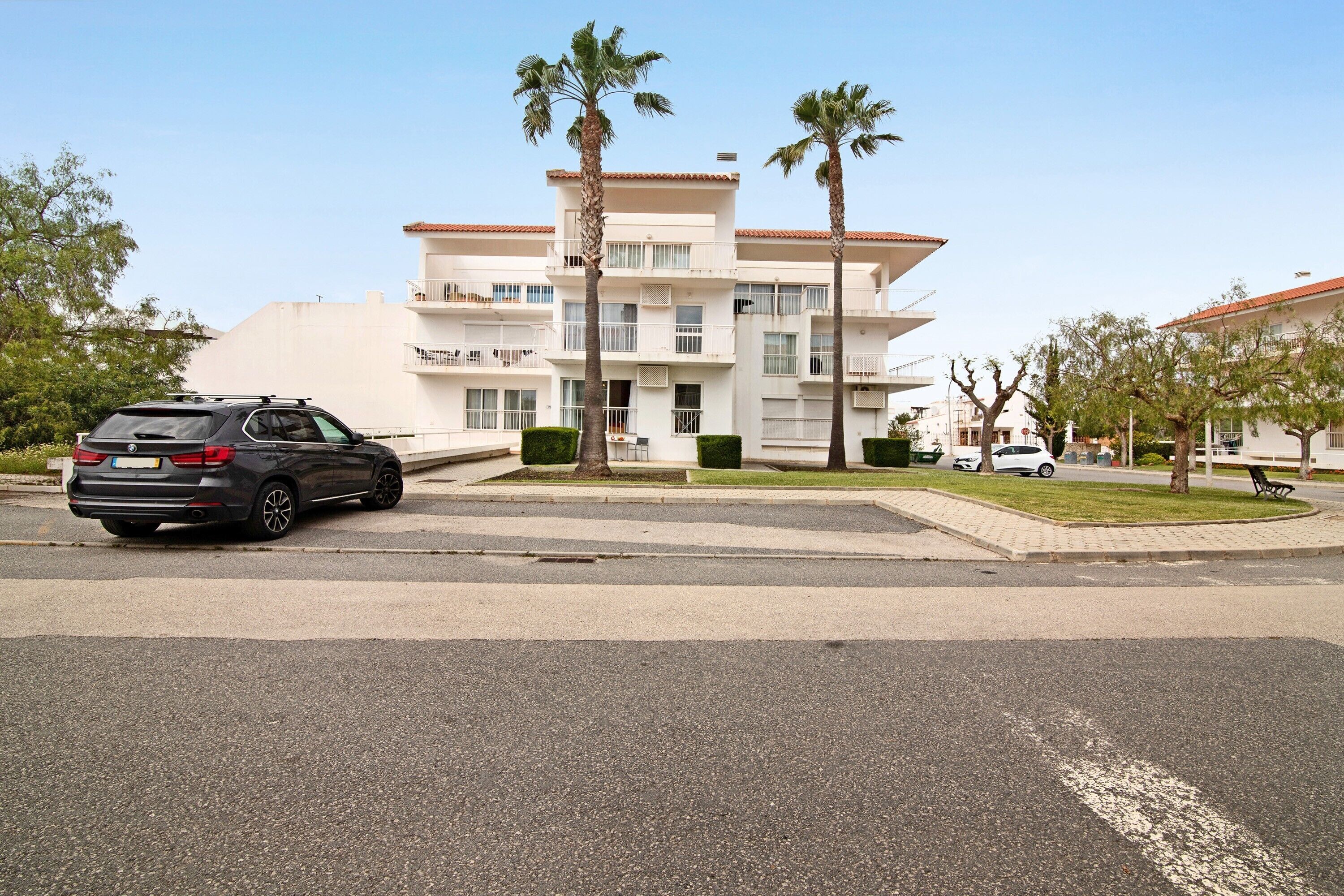 Un immeuble à plusieurs étages, doté de balcons, de palmiers et d’une voiture garée.